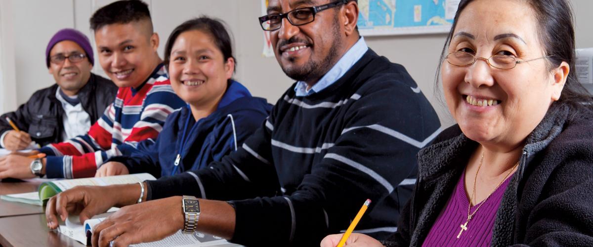 A diverse groups of students sitting at table and smiling at camera